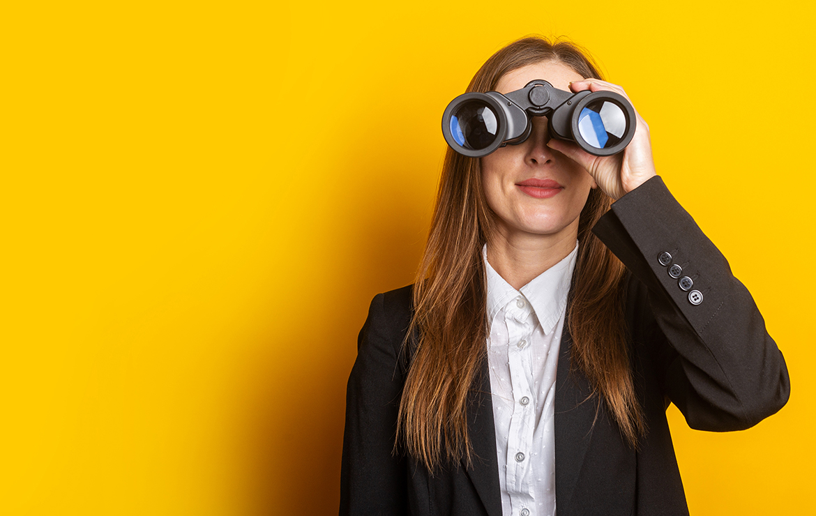 smiling young business woman looking through binoculars on yellow background